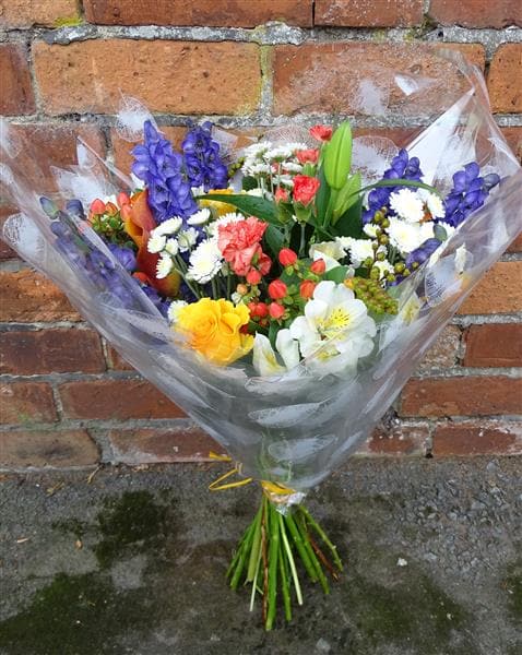 This vibrant bouquet beautifully combines orange, white and purple flowers to make a simple and stylish gift. It includes a white Lily, Hypericum Berries, Chrysanthemums and Roses, with seasonal flowers. A beautiful present for a birthday or Thank You.