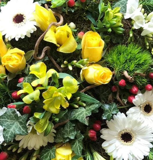 This woodland grouped posy funeral tribute is based on moss and has lots of natural material detail including flowers, foliage, buds, berries, ivy trails, and twisted hazel sticks.
