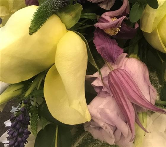 This based wreath funeral tribute is created by closely packing white Chrysanthemums together and contoured to create a soft ring of flowers. It is finished off with a spray of lemon and lilac seasonal flowers and foliages to create a delicate finish to fit your personal taste.