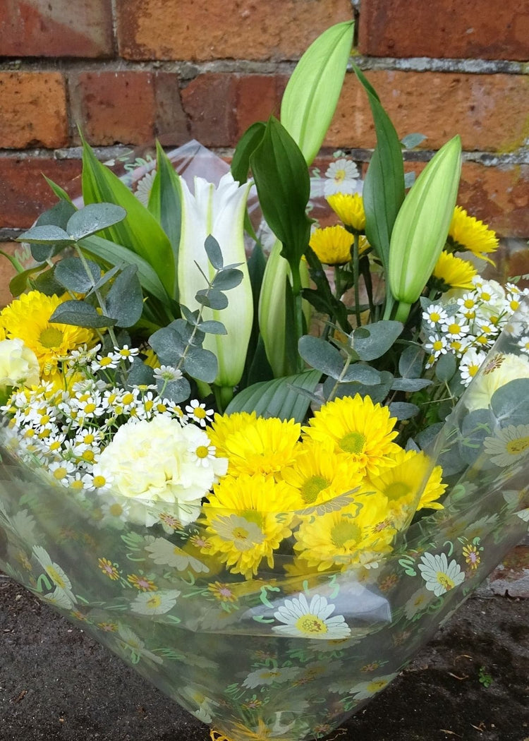 Chamomile Hand Tied Bouquet. This fresh, zesty bouquet beautifully combines yellow and white flowers to make a simple and stylish gift. It includes a white Lily, Carnations, Chrysanthemums, with seasonal flowers. A beautiful anniversary, birthday or Just to Say... gift.