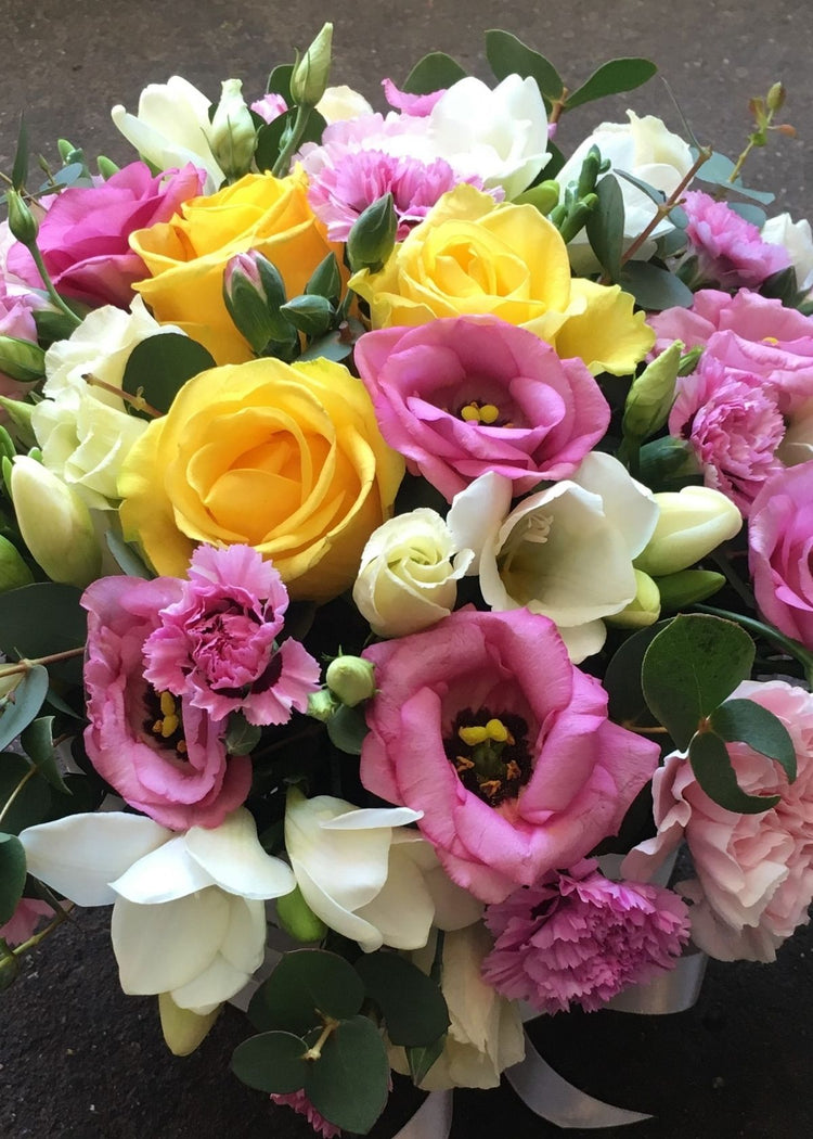A compact posy funeral arrangement of pink, yellow and white shades filled with Freesias, Lisianthus, Carnations, Roses and seasonal flowers and foliage by Make Their Day florist.  This funeral tribute is 12" (31cm) approx. diameter and is most suitable from a family member or a close friend to a lady of any age.