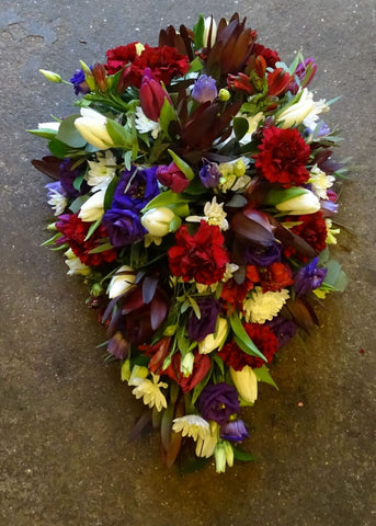 This funeral casket spray is a loose, single ended teardrop shape, fashioned from rich red and purple tones by Make Their Day florist.  If there is a favourite flower that you would like included, we will do our best to supply it. Please call or visit us to place your order. We will let you know if a specific flower will incur an additional cost when we take your order.