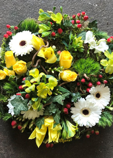 This woodland grouped posy funeral tribute is based on moss and has lots of natural material detail including flowers, foliage, buds, berries, ivy trails, and twisted hazel sticks.