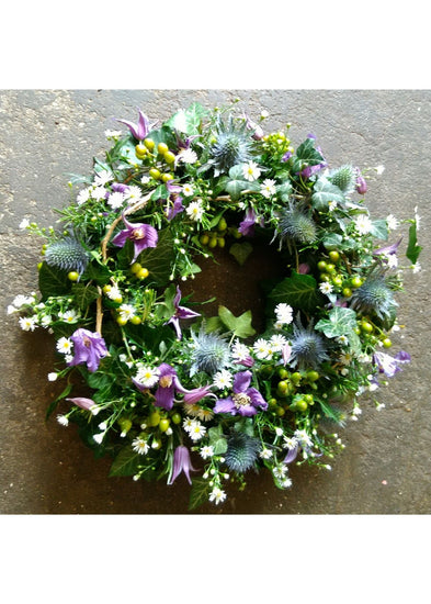 The Cotswold Funeral Wreath by Make Their Day florist. This detailed modern, textured funeral wreath is filled with Clematis, September Flower, Eryngium, green Hypericum berries, twigs, and seasonal foliages. This loose design showcases this beautiful medley of colours and textures.