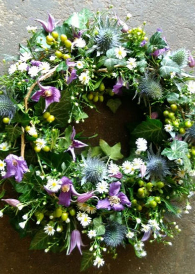 The Cotswold Funeral Wreath by Make Their Day florist. This detailed modern, textured funeral wreath is filled with Clematis, September Flower, Eryngium, green Hypericum berries, twigs, and seasonal foliages. This loose design showcases this beautiful medley of colours and textures.