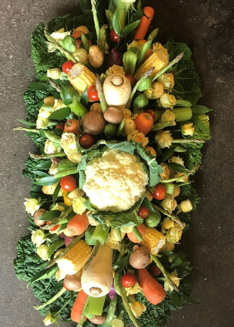 A funeral casket spray made of seasonal vegetables and yellow Roses.