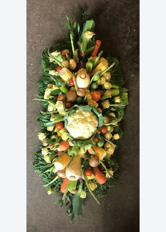 A funeral casket spray made of seasonal vegetables and yellow Roses.