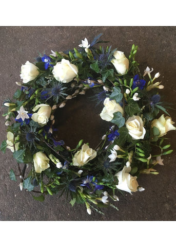 This detailed modern, textured Woodland Walk funeral wreath by Make Their Day florist, is filled with blue and white Roses, Freesia, Eryngium, Delphinium, lavender and seasonal twigs and foliages. This loose design showcases this beautiful medley of a Cotswold countryside walk in colours and textures.