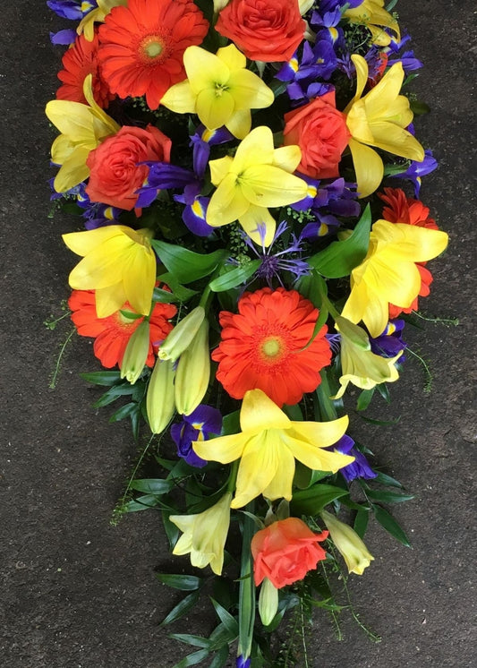 This cheerful, single ended funeral spray is full of yellow, orange and purple including Lilies, Roses, Germinis and Irises.