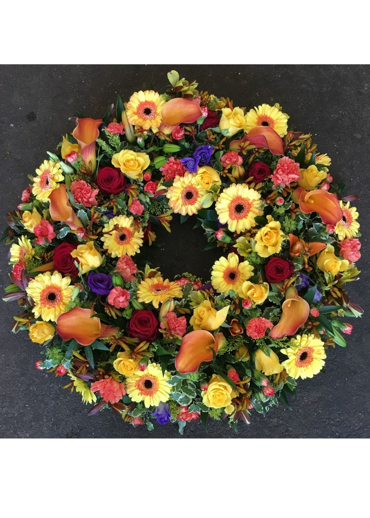 Yellow and Orange Loose Funeral Wreath by Make Their Day florist. This traditional funeral wreath combines Yellow Germinis, and Roses coupled with orange Carnations, purple Lisianthus with seasonal flowers and foliages.