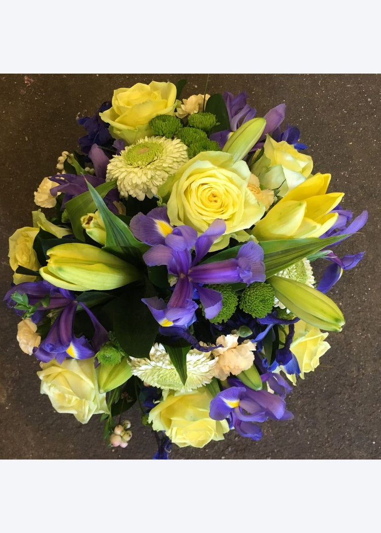 A bright posy funeral tribute of yellow and blue flowers by Make Their Day florist. It includes Roses, Chrysanthemums and Irises and other seasonal flowers and foliage.  The standard price is for an 14" (36cm) posy and is suitable from a family member, friend, work colleague or neighbour for a lady or gentleman.